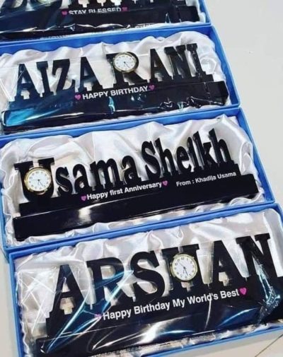 Acrylic Customized Name Clock made up of Black Acrylic which is cut into customized names and has a clock in it. It also includes a customized text. The picture has 4 different Acrylic Customized Name Clocks, packed in a box with white silk cloth.