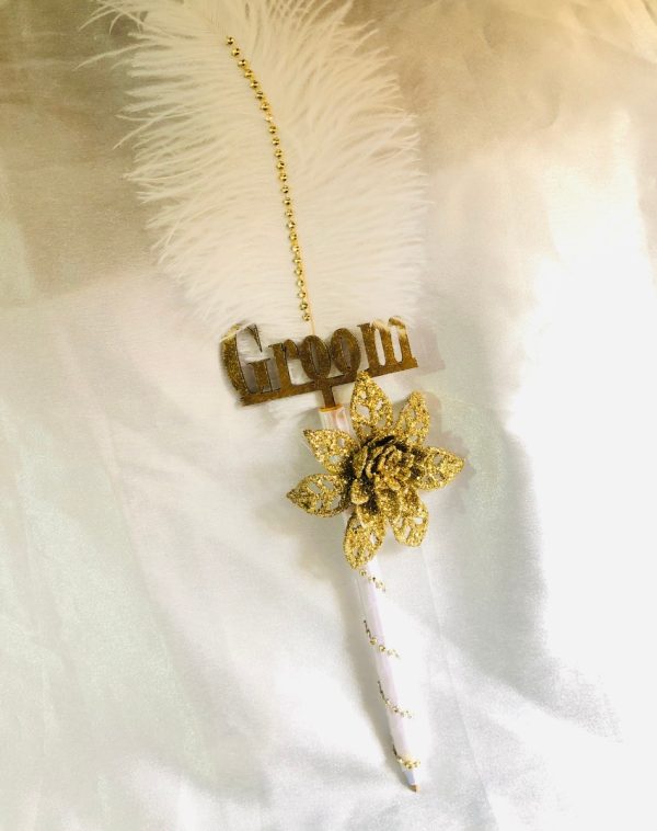 White feathered Nikkah Pen For Groom, with Groom written in gold color. It also has a gold flower on it..