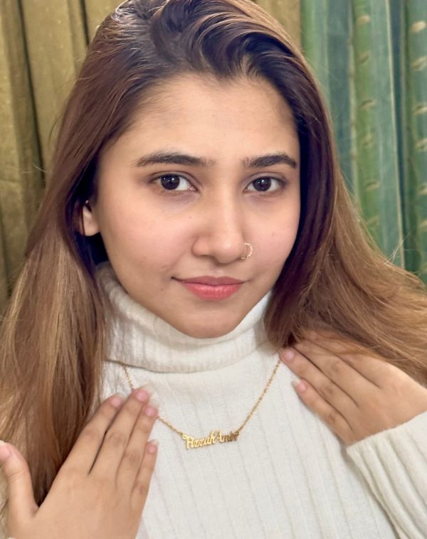 Close-up of Fizzah Amir wearing the Double Name Gold-Plated Necklace, her hands delicately placed on her chest, showcasing the personalized name pendant. She's wearing a white ribbed turtleneck.