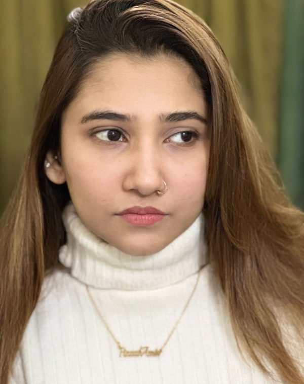 Fizzah Amir wearing the Double Name Gold-Plated Necklace, her gaze turned to the side, showcasing the personalized pendant against a white ribbed turtleneck.