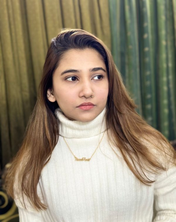 Fizzah Amir wearing the Double Name Gold-Plated Necklace, posing with a side gaze against a backdrop of curtains.