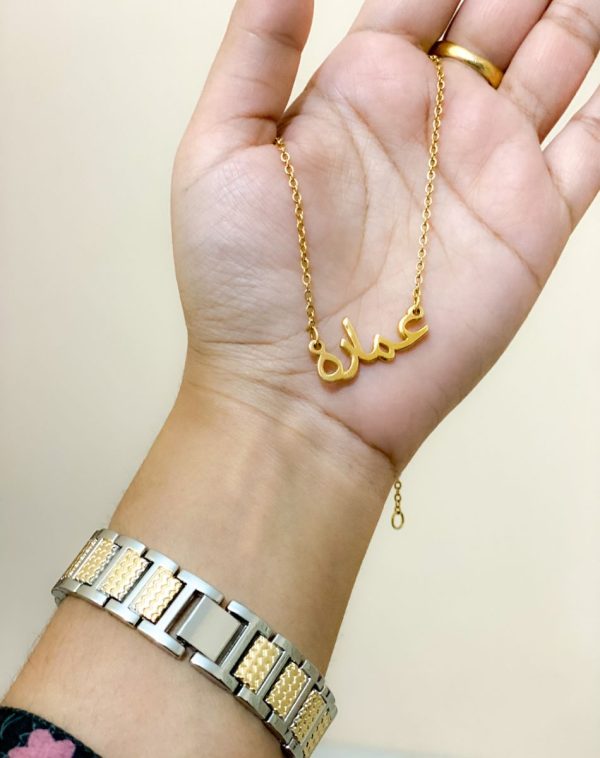 Hands showcasing a gold-plated necklace with the name "Ammara" written in Arabic script.