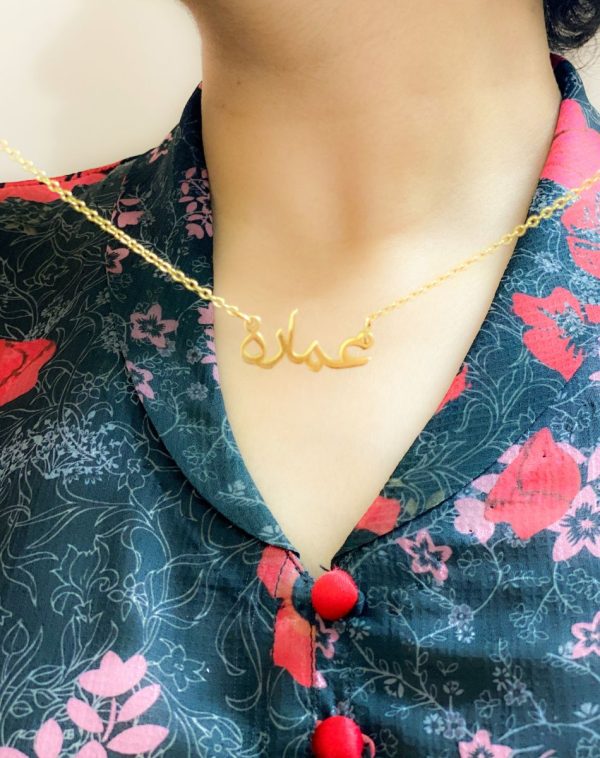 Close-up shot of the Single Arabic Name Gold-Plated Necklace, featuring the customized name pendant "Ammara" worn by influencer Ammara. She is dressed in a floral pajama shirt, adding a touch of casual elegance to the image.