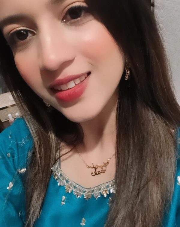 Shahnila Jibran wearing Double Arabic Name Gold-Plated Necklace, a close-up selfie with a tilted head and a bright smile.
