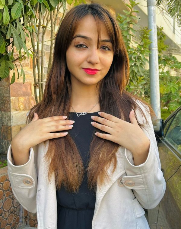 Influencer Muqaddas confidently showcases our Single Arabic Name Silver-Plated Necklace, wearing a pink jacket with a black inner. Her hands gracefully rest on her chest, drawing attention to the necklace.