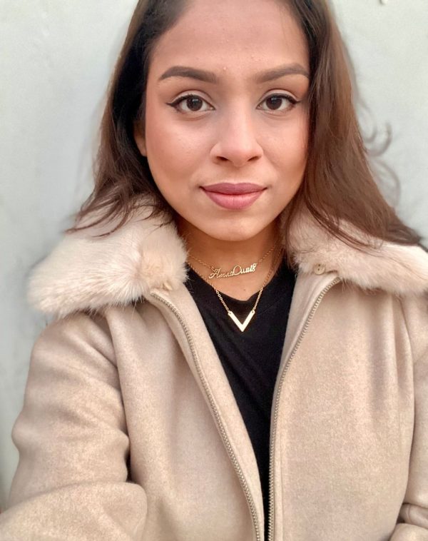 Influencer Amna Owais wearing our Double Name Double Chain Gold-plated necklace, taking a selfie. The background is white, and she is wearing a fur jacket in a skin color tone and a plain t-shirt.