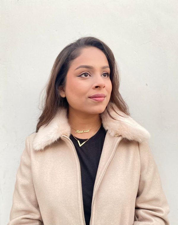 Influencer Amna Owais showcasing our Double Name Double Chain Gold-plated necklace from the side, wearing a skin color fur jacket and a plain t-shirt.