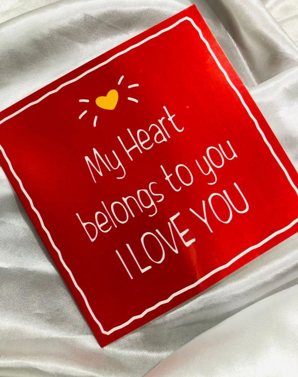 A red Marks and Spencer greeting card with a small yellow heart at the top and 3 white lines on each side resembling sun rays. The text "My heart belongs to you, I Love You" is written in white color.