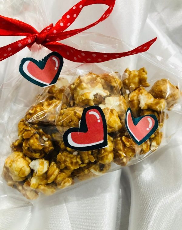 A Transparent Bag of Salted Caramel Popcorn wrapped with Red Polka Dots Ribbon and is decorated by mini red heart stickers.