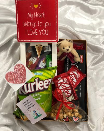 A Valentine's Day Munch Box filled with a variety of delicious snacks including chips, coffee and chocolate-filled cookies, KitKat chocolate, and mini cones with different flavors. It also comes with Salted Caramel Popcorn, a teddy bear, and a Valentine's Day greeting card, making it an affordable and thoughtful gift option for your partner.