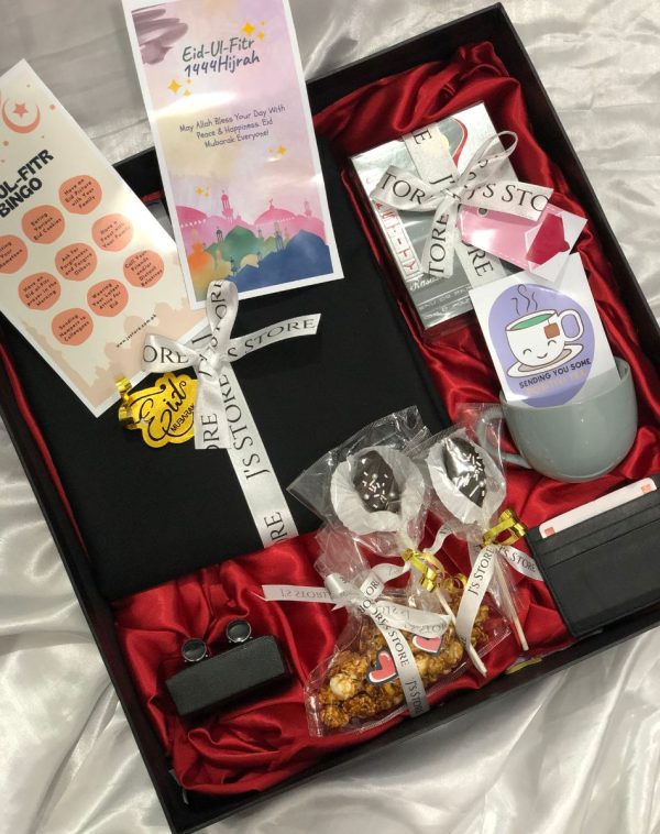 A curated gift box with various items for Eid celebrations, including an unstitched Shalwar Kameez suit, perfume, marble cufflinks, a leather cardholder, two chocolate coated date pops, a bag of salted caramel popcorn, a teacup with tea bags, an Eid bingo game, and an Eid greeting card. The Festive Eid Box comes in a 16 * 16 inches curated box with Imported Shredded Papers, ribbons, mini cards, and more, making it a beautiful and thoughtful gift.