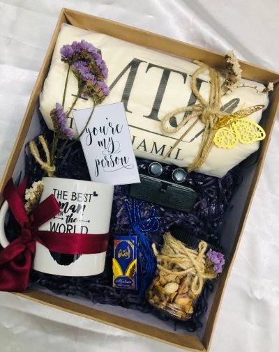 A gift set including a men's unstitched shalwar kameez, customized mug, nuts jar, black marble cufflinks, tasbeeh, and itr, beautifully arranged in a curated box with ribbons and mini cards.