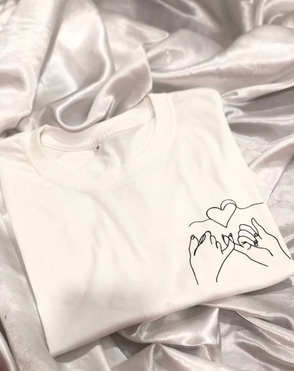 A white crew-neck T-shirt features a black line art print of two hands reaching and intertwining to form a delicate heart shape. This is the J's Store Heart Line Art T-Shirt for men.