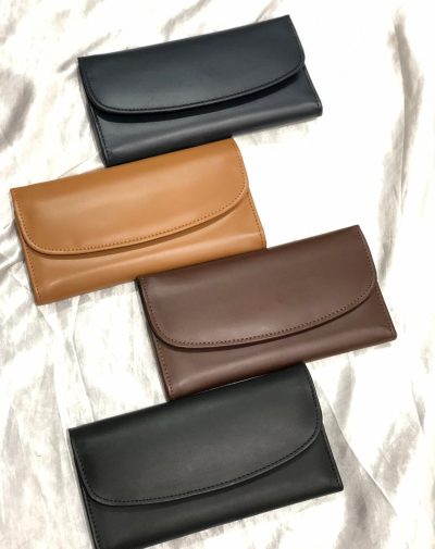 Four bridle leather trifold wallets in black, dark brown, camel, and navy blue on a white fabric.