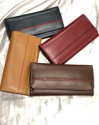 Four Timeless Leather Wallets in Blue, Dark Brown, Camel, and Red displayed on a soft white fabric.