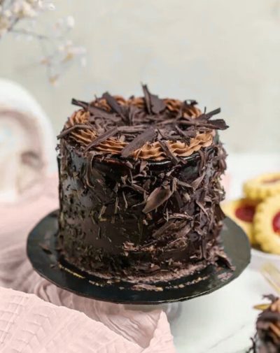 Chocolate Devils Mini Cake by J’s Store with chocolate frosting and flakes on a black base.