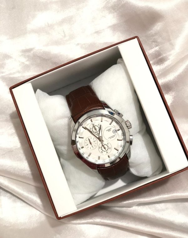 The SuperSport Chrono Watch in a box. The watch has a white face with silver and black dials and a brown leather strap.