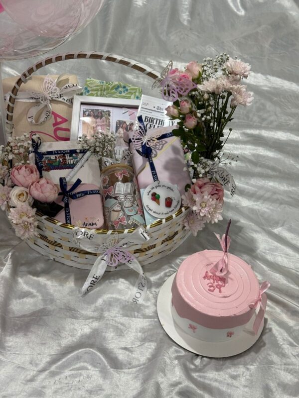 The Grand Wardrobe & Keepsake flat lay view featuring handcrafted wooden basket 3-piece lawn suit custom glass tumbler travel jewelry organizer and fresh cake from J's Store