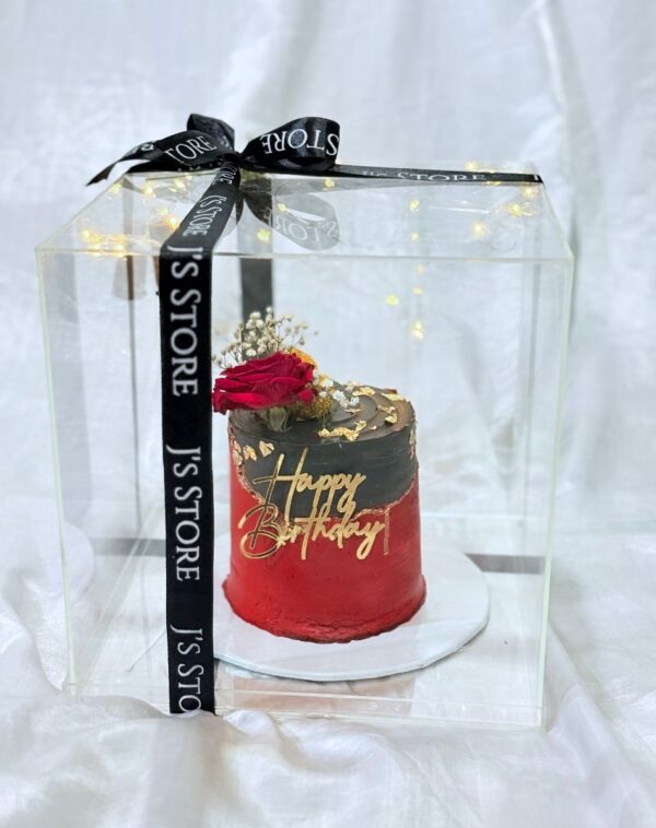 Custom black and red cake with gold leaf and fresh rose inside a fairy-lit clear acrylic box from J's Store included in The Royal Crimson Suite